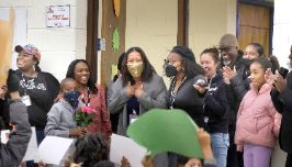 African American female enters gym door shocked as family, staff and students cheer for her